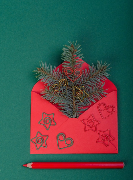 red envelope with a Christmas tree branch, next to a red pencil.