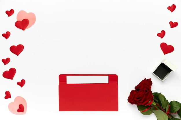 Red envelope with letter, bouquet of roses, many hearts and box for ring on white background. Top view, flat lay