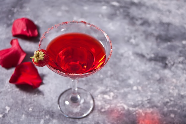 Red exotic alcoholic cocktail in clear glass and red roses petal on the concrete for romantic dinner. Copy space.