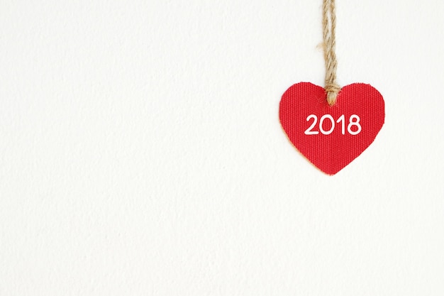 Red fabric heart shape with 2018 word hanging on the clothesline over white wall background