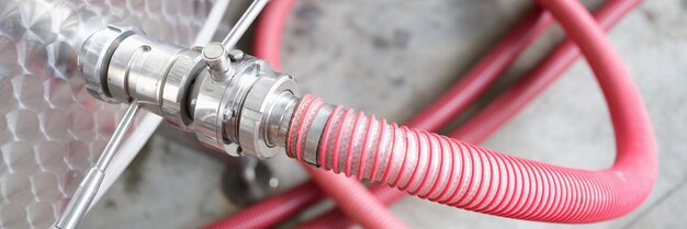 Red faucet connected to steel barrel in factory closeup