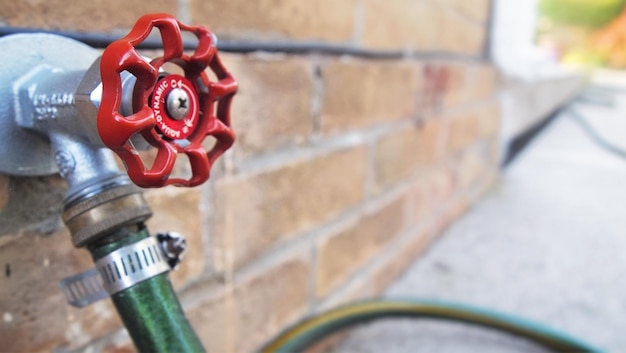 Red faucet for garden house along a brick wall