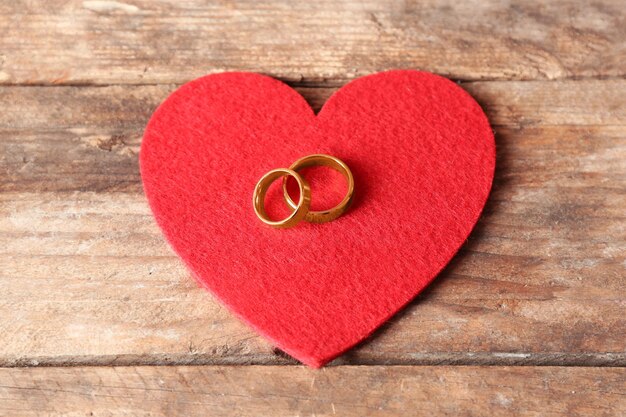 Red felt heart and wedding rings on wooden background closeup