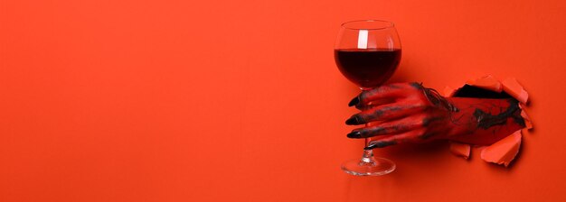 Red female hand with glass of wine on red background space for text