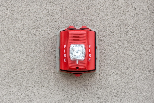 Photo red fire alarm siren with flashing light strobe isolated on gray cement wall outdoor fire safety