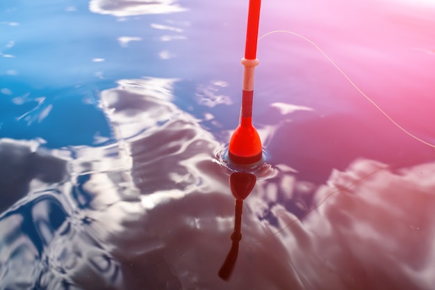 Red fishing float floats on water in which clouds are reflected