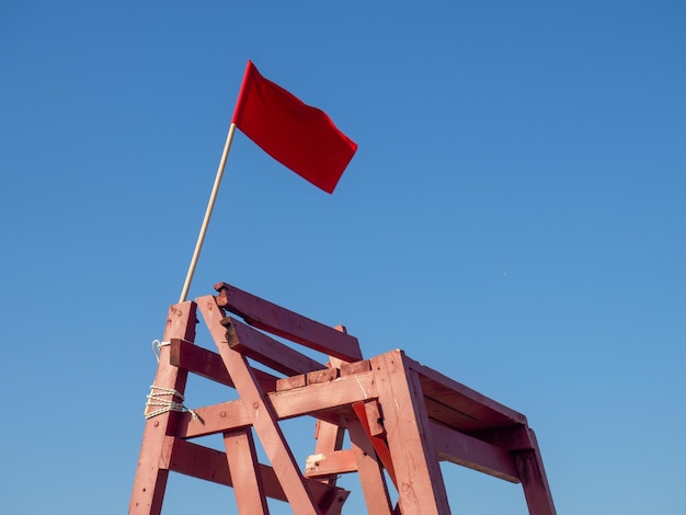 Red flag on a wooden platform flag as a symbol of danger bathing is prohibited beach on the sea the concept of rescue work beach safety