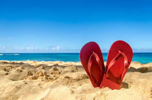 Foto flip-flop rossi sulla spiaggia sabbiosa