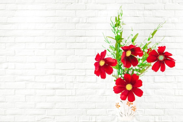白いレンガの背景に赤い花と緑の植物