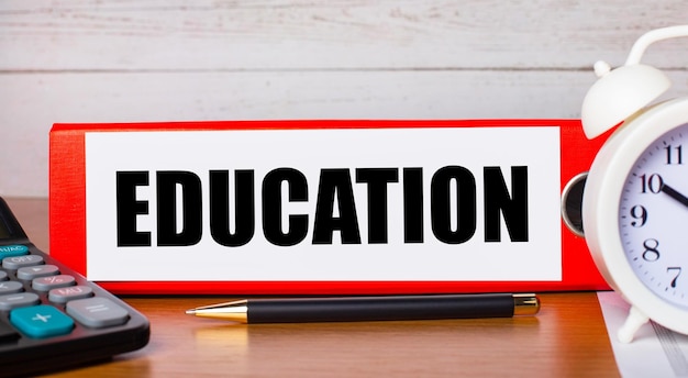 red folder for papers with the text education white alarm clock calculator and pen on the desktop business concept