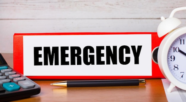 red folder for papers with the text emergency white alarm clock calculator and pen on the desktop business concept