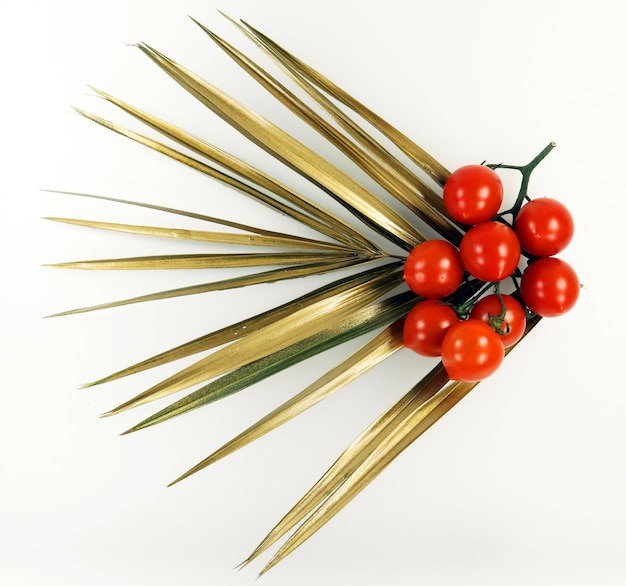 Red fresh appetizing cherry tomatoes and a golden palm leaf on white background close-up.