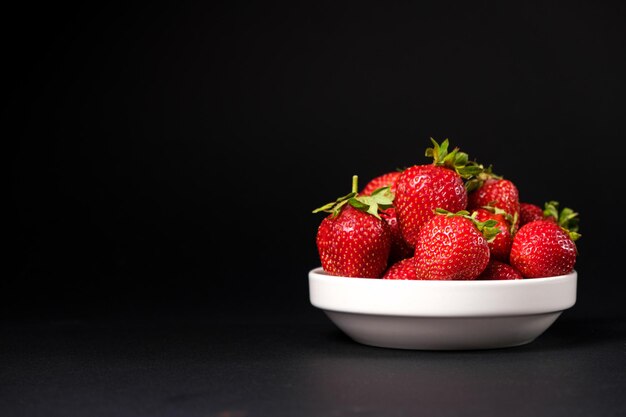 Red fresh strawberries in a white plate on a black background Summer seasonal berries closeup