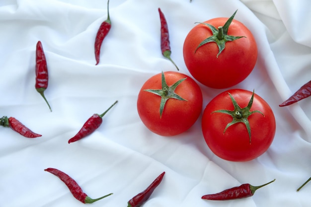 Red fresh tomatoes among chilli peppers on the white fabric