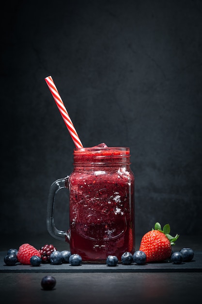 Red fruits smoothie and berries on dark background