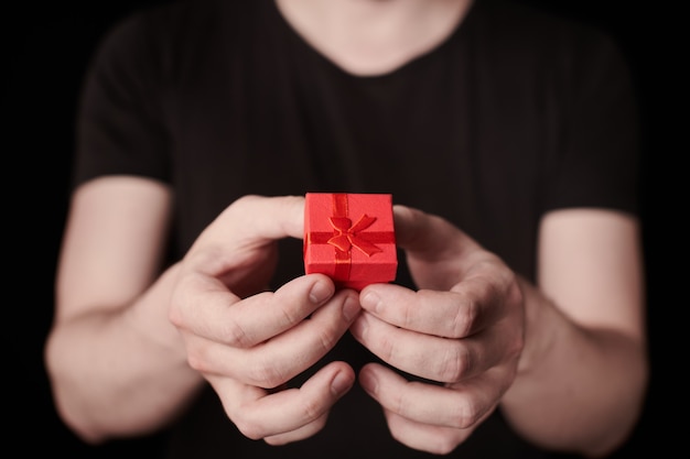 Red gift box in hand. valentine gift. small anniversary giftbox\
from man. little surprise concept. black background.