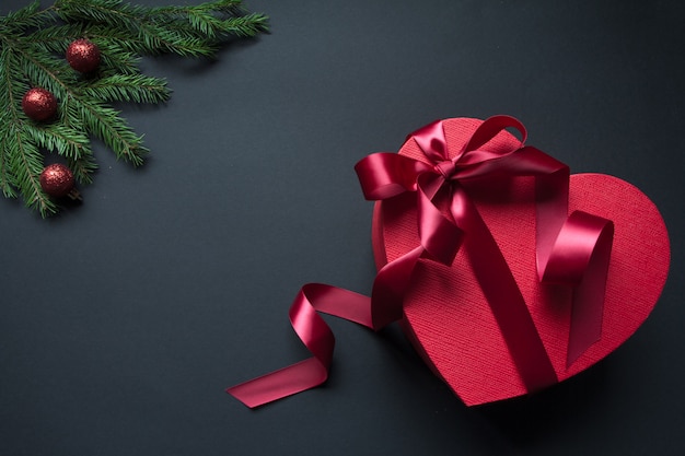 Red gift box heart shape with red ribbon and decorated Christmas tree branches