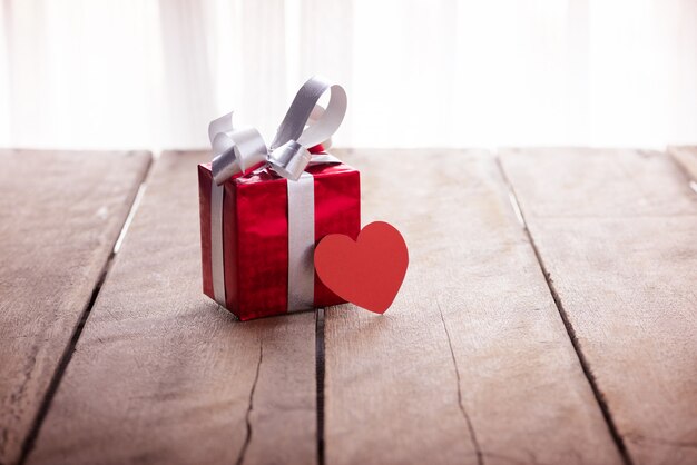 Red gift box and heart on white wooden table