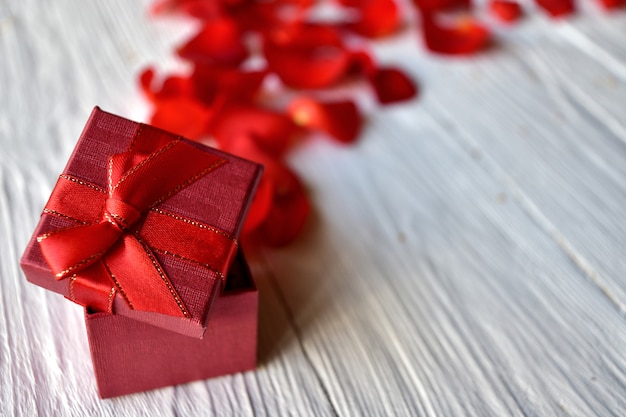 Red gift box and red rose petals on a white wooden. Valentine's Day concept