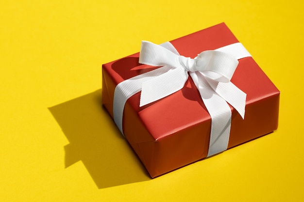 Red gift box tied with white ribbon on isolated on yellow background
