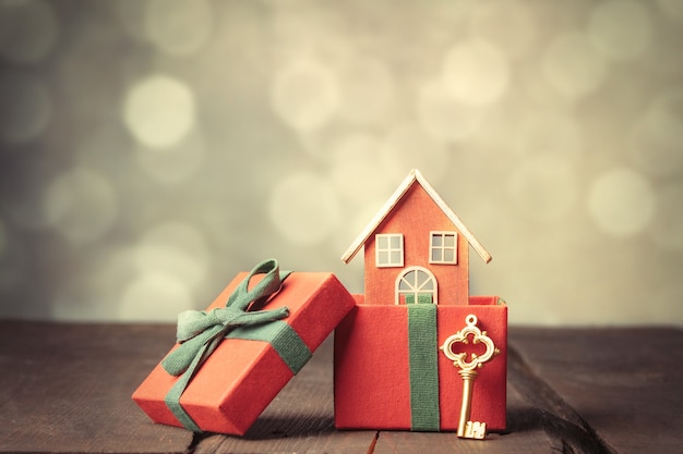 Red gift box and toy house on wooden table with bokeh on background.