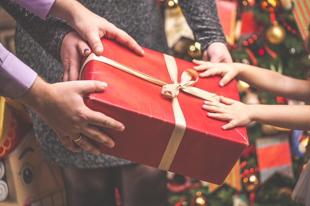 Red gift box with all family hands against Christmas tree. 