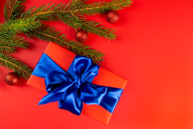 Red gift box with a blue bow near fir branches on a red . a Christmas gift