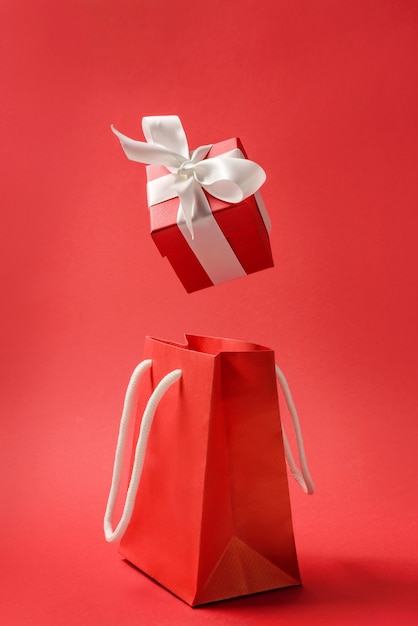 Red gift box with a bow falls into a paper bag. Gift shopping concept.