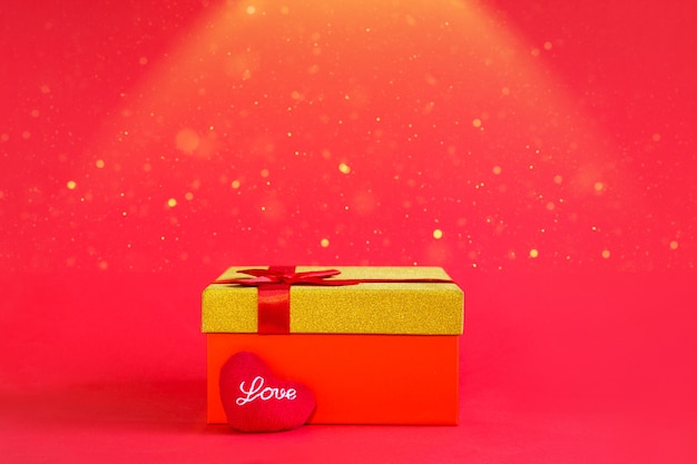 Red gift box with a bow and a soft heart with the inscription Love