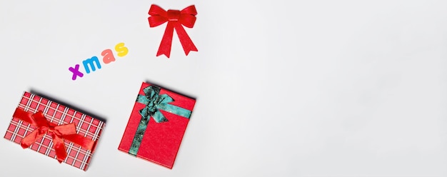 Red gift box with a green ribbon and a red bow with the inscription Xmas on a white background New year christmas concept Flat lay festive mockup with copy space