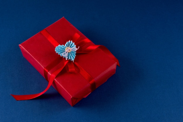 Красная подарочная коробка с сердцем и бантом на классическом синем фоне цвета 2020. Концепция упаковки дня святого валентина 14 февраля. Плоская планировка, копия пространства, вид сверху.