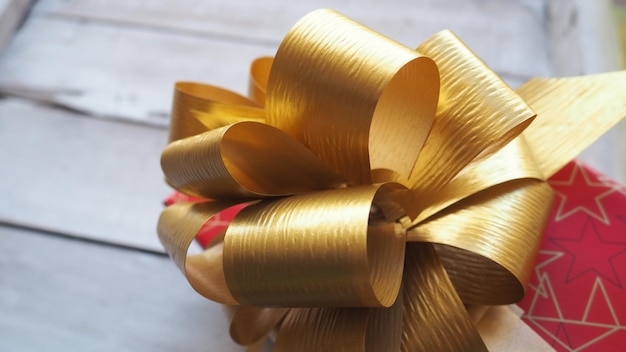 Red gift box with a large gold bow on a wooden background painted with white paint Gift