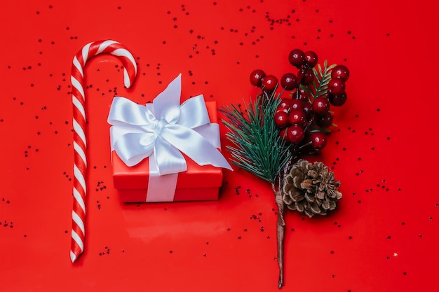 Red gift box with a white bow on a red background with candy and fir branches.