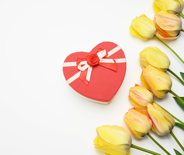 Red gift box and yellow tulips on white surface, festive surface, top view