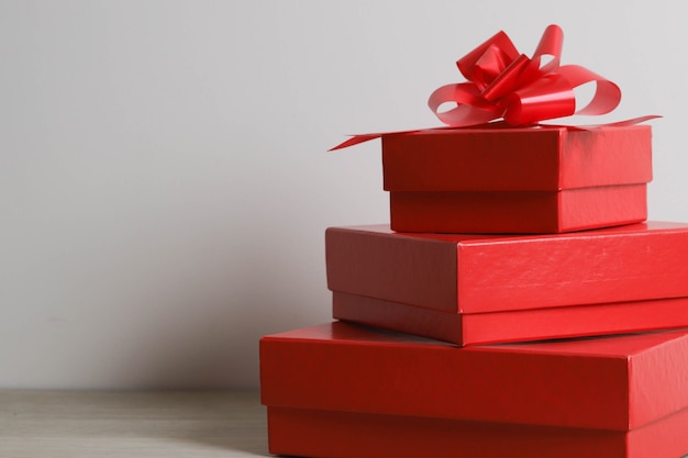 Red gift boxes and red ribbon on wooden background with space.