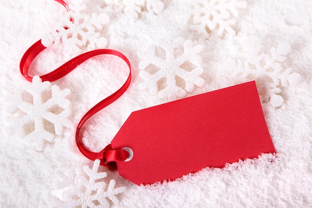 Red gift tag or price ticket with red ribbon in a snow background.