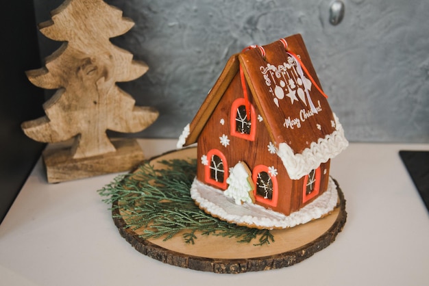 Foto red gingerbread house, concetto di vacanza di natale e felice anno nuovo. casa di pan di zenzero fatta in casa con finestre di caramelle su un tavolo di legno con decorazioni natalizie. atmosfera vacanziera