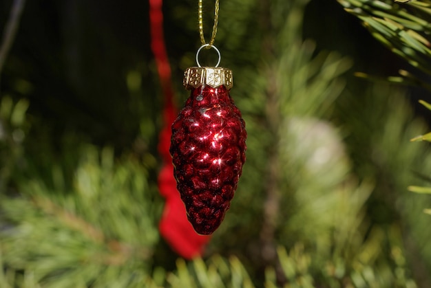 Red glass Christmas tree decoration in the shape of fir cone on a background of a Christmas tree