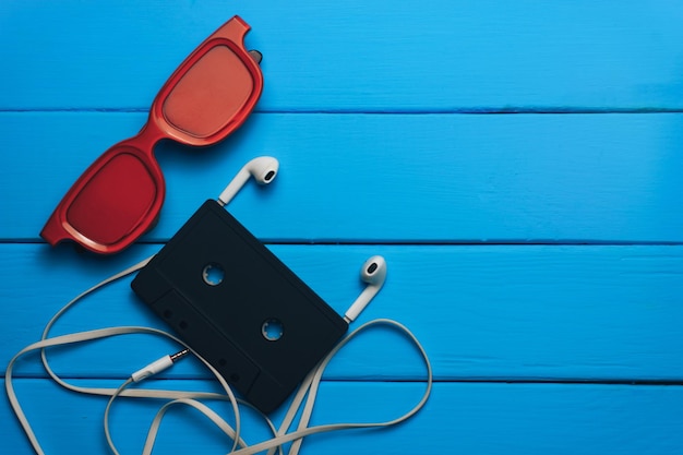 red glasses classic magnetic cassette tape and white headphones on a blue wooden table background