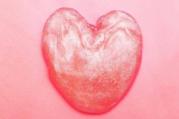 Red glitter slime in the form of a heart on pink background