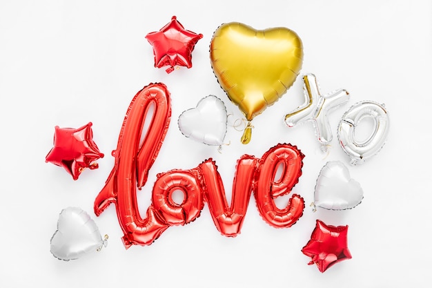 Красные и золотые шары фольги в форме слова «Любовь» с сердечками на белом фоне. Концепция любви. Праздник, торжество. День святого Валентина или украшение свадьбы / девичника.