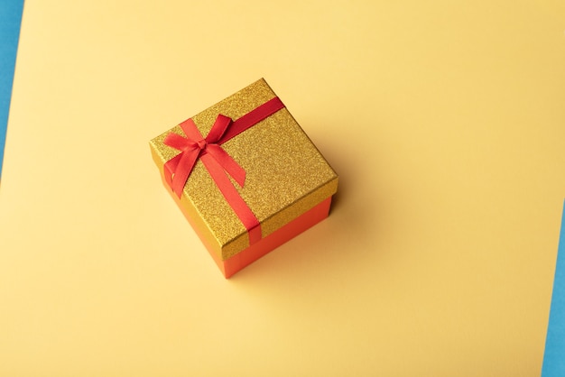 Red and gold gift box with a red ribbon on a yellow background