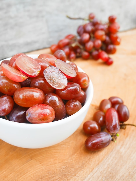 Red grape in the white bowl on the wooden background.