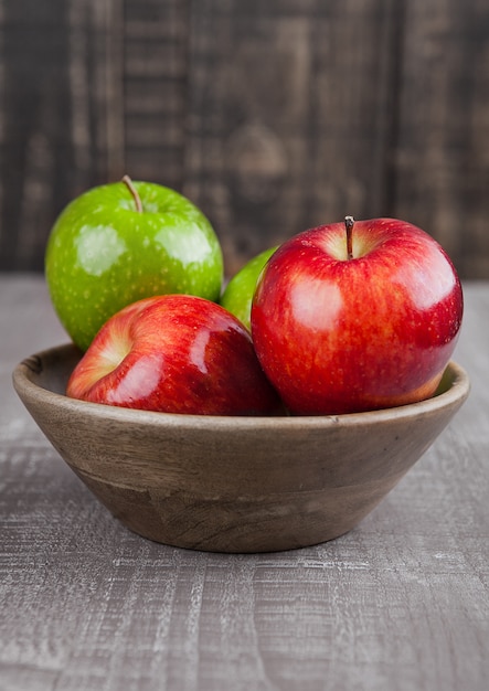 Red and green apples in wooden bowl on wooden board