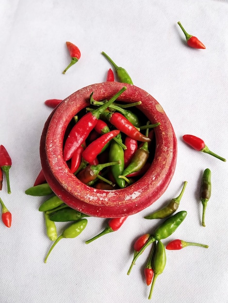 Photo red and green chilli in a red colored crock (mud made pot) in a white table