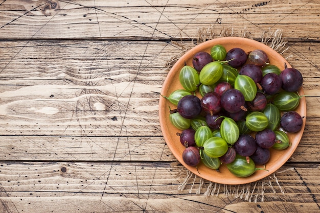 Red and green gooseberry berries in a plate on a wooden surface