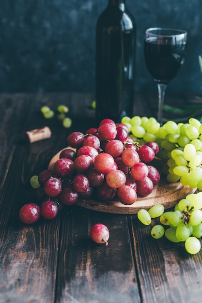 赤と緑のブドウと木製のテーブルの上のグラスのワイン