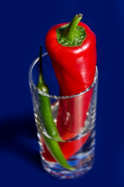 Photo red and green peppers in a slightly filled glass cup with a dry tail