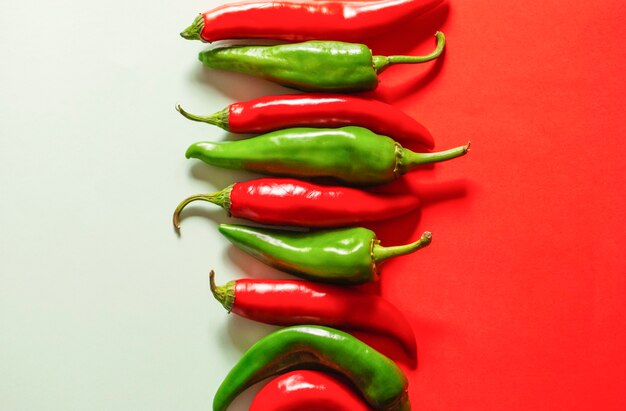 Red and green peppers on a white-red surface next to each other.
