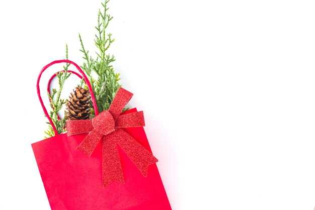 Red and green shopping bags with Christmas decoration, fir tree branches, festive bow  isolated on white background top view copy space. Xmas sale concept